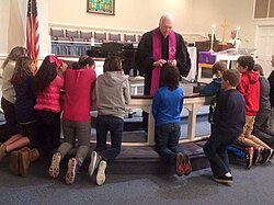 A Methodist minister distributing ashes to confirmands kneeling at the chancel rails on Ash Wednesday