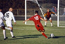 The striker (wearing the red shirt) is past the defence (in the white shirts) and is about to take a shot at the goal.