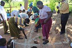 A health worker (centre) gets villagers to draw a map of the area, showing the main features like the road and the river (a village near Lake Malawi, Malawi).