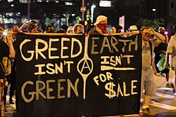 Anarchist protesters against capitalism, with a sign reading "Greed isn't Green"
