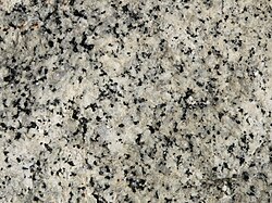 A closeup of the polished face of a slab of granite showing grains of white, bluish gray and black.