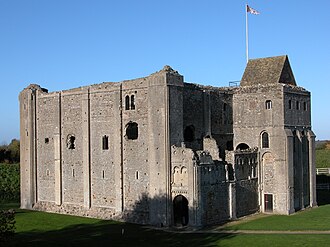 A square building of grey stone with narrow vertical slits on the first floor, and wider windows on the second. The top of the castle looks decayed and there is no roof, except over a tower attached to the keep.