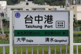 A sign for Taichung Port railway station in Taiwan with writing using traditional characters, English, Wade–Giles (Taichung), and pinyin