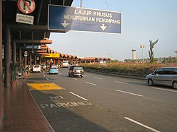 Indonesian road signs in Soekarno–Hatta International Airport. The blue sign reads "Lajur Khusus Menurunkan Penumpang" which means "Lane for dropping passengers only" and the small no-parking sign on the left reads "Sampai Rambu Berikutnya" which means "until next sign" in Indonesian.