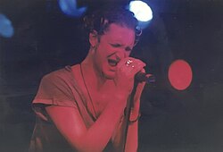 A male singer, Layne Staley, performs onstage with Alice in Chains. He holds the microphone with both hands and his eyes are closed as he sings.