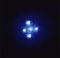 In the formation known as Einstein's Cross, four images of the same distant quasar appear around a foreground galaxy due to strong gravitational lensing.