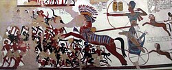 Ramesses II in his war chariot charging into battle against the Nubians. New Kingdom reliefs as seen in Rameses II temple, Beit el-Wali, represented Nubians with dark reddish brown and jet black skin tones.[111]