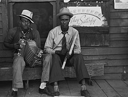 Early Creole musicians playing an accordion and a washboard in front of a store, near Opelousas, Louisiana (1938).