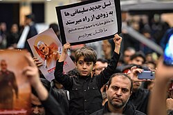 A boy holding a paper stating "we are the killers of the Jews" in the mourning ceremony for Qasem Soleimani at Mosalla of Tehran, 6 January 2020