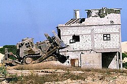 An IDF Caterpillar D9 armored bulldozer demolishing a house in the Gaza Strip during the Second Intifada