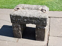 A large grey stone with two rings attached, propped up on two smaller stones.