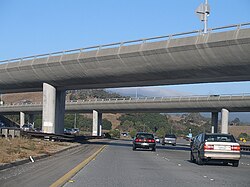 A freeway with several cars driving on it, with two concrete bridges passing overhead