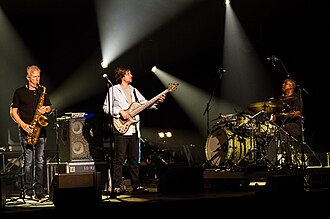 As this photo shows, popular music genre bands use acoustic instruments (such as sax and drums) and electric instruments (such as electric bass), all of which are amplified through a PA system of speakers. Pictured are the Yellowjackets, a jazz-rock fusion band.