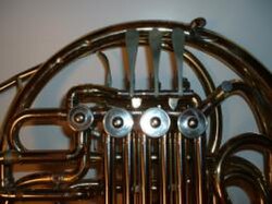 The valves of a Conn 6D double horn. The three lever keys (above the large valves) can be depressed toward the large outer tube. The thumb key (near the left-most valve) moves inward toward the three finger keys.