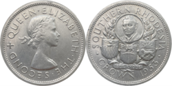 Silver coin: 1 crown Southern Rhodesia; Bust of Cecil John Rhodes, the Prime Minister of the Cape Colony, colonial magnate, and namesake of Southern Rhodesia, in a circle in the center and three shields for each colony developed by Rhodes, representing (from left to right) Northern Rhodesia, Southern Rhodesia, and Nyasaland below, all flanked by two wreaths wrapped in banners