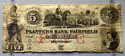 Five-dollar banknote showing a plantation scene with enslaved people in South Carolina. Issued by the Planters Bank, Winnsboro, 1853. On display at the British Museum in London.