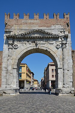 Roman triumphal arch in Italy with modern buildings in the background