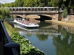 One of Strasbourg's trams passes over one of its canals, while a tourist trip boat passes underneath.