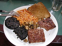 Scottish-style cooked breakfast, centred around black pudding (left), served with square sausage, baked beans, mushrooms, and fried bread
