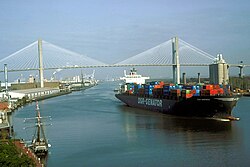 A container ship leaves the Port of Savannah after passing under the Talmadge Memorial Bridge and proceeding east down the Savannah River past the Savannah Historic District.