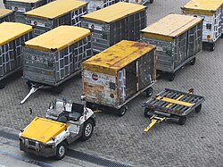 A single trailer for an aircraft cargo unit load device, next to a group of trailers for loose luggage