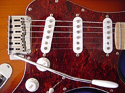 This Squier Stratocaster has features common to many electric guitars: multiple pickups, a vibrato bar/vibrato unit, and volume and tone knobs.