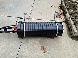An aerial optical fiber splice enclosure lowered during installation. The individual fibers are fused and stored within the enclosure for protection from damage.