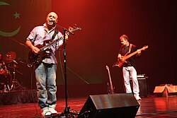 Junoon performing live with the national flag of Pakistan displayed in the background.