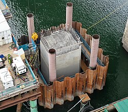 A large concrete structure in the middle of a river, kept dry by a steel wall surrounding it