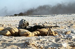 A Syrian soldier aims a 7.62mm PKM light machine gun from his position in a foxhole during a firepower demonstration, part of Operation Desert Shield. The soldier is wearing a ShMS gas-mask.