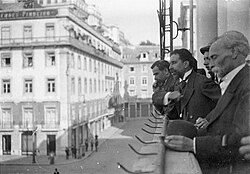 Black-and-white photograph of José Relvas proclaiming the Republic together with several formally dressed men leaning over the balcony railing of Lisbon City Hall and looking down onto a square surrounded with buildings.