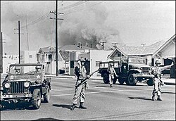Soldiers direct traffic away from an area of South Central Los Angeles burning during the 1965 Watts riot