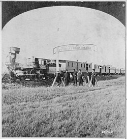 Directors of the Union Pacific Railroad gather on the 100th meridian, which later became Cozad, Nebraska, about 250 miles (400 km) west of Omaha in the Nebraska Territory, in October 1866. The train in the background awaits the party of Eastern capitalists, newspapermen, and other prominent figures invited by the railroad executives.