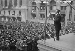 Edge addressing a large crowd during World War I. Liberty bond banners adorn a nearby building.