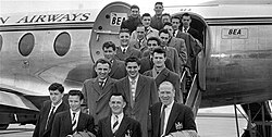 A black-and-white photograph of several people in suits and overcoats on the steps of an aircraft.