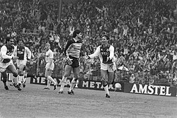 Van Basten celebrates his goal for Ajax to give the team a 2–0 lead in an eventual 8–2 win against Feyenoord in September 1983, following Gerald Vanenburg's corner. Edo Ophof (Ajax), Felix Gasselich (Ajax), André Hoekstra (Feyenoord) and goalkeeper Joop Hiele (Feyenoord) are the other players in the picture. The average age of the Ajax team at the time was roughly 22+1⁄2 years.[12]