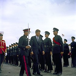 John Fitzgerald Kennedy, escorted by a Bermuda Militia Artillery officer in Royal Artillery blue No. 1 Dress, inspects green-uniformed riflemen of the Bermuda Rifles in 1961