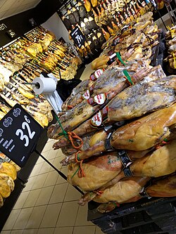 Large stacks of cured jamón legs displayed for sale in a Spanish supermarket, each priced at 32 euros