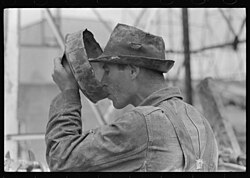 A Lone Driller's Water Break drinking from a battered pan during the Texas oil boom in Kilgore, Texas, 1939
