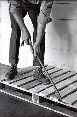 A man using a crowbar to dismantle a wooden pallet
