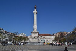 Photograph of a white stone column with a man wearing a laurel wreath and military dress and who holds forth a scrolled sheaf of paper on the top