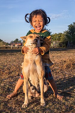 A young girl from Laos laughing while hugging her dog