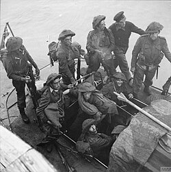 nine British soldiers and one sailor on a small boat at sea. A Union Jack flies from a mast at the rear.