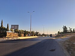 The entrance to the city of Aleppo from the M5 motorway. This section features two lanes in each direction, separated by a curbed median strip with arched-arm streetlight poles.