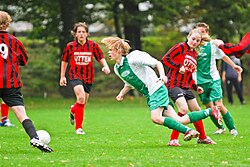 A player (red/black) commits a foul by tripping her opponent (green/white).