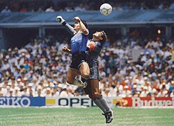 Maradona flicks the ball with his hand past the outstretched arm of Peter Shilton, also known as the "Hand of God"