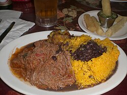 A traditional meal of ropa vieja (shredded flank steak in a tomato sauce base), black beans, yellow rice, plantains and fried yuca with beer