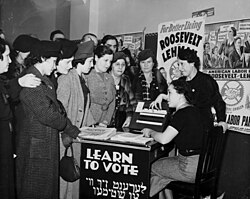 Women surrounded by posters in English and Yiddish supporting Democratic candidates Franklin D. Roosevelt, Herbert H. Lehman, and the American Labor Party teach other women how to vote, 1936.