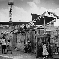 Slum (bohío) dwellings in Havana, Cuba in 1954, just outside Havana baseball stadium. In the background is advertising for a nearby casino.
