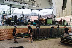 A team of roadies carries music gear, sets up equipment, and readies the stage for the band's show.